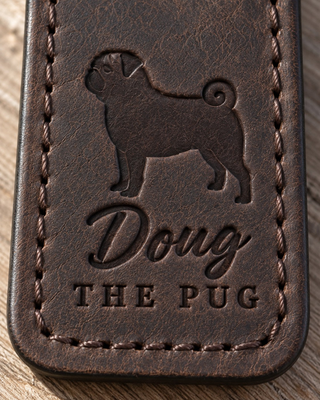 Close-up of the name Doug and THE PUG pressed into dark brown full-grain leather under a pug silhouette