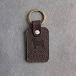 Dark espresso leather keychain debossed with a curly-tailed pug above Best friend and THE PUG, on gray concrete