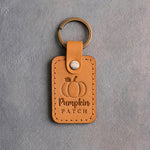 Indian Summer tan leather keychain debossed with a pumpkin above Pumpkin PATCH, on gray concrete