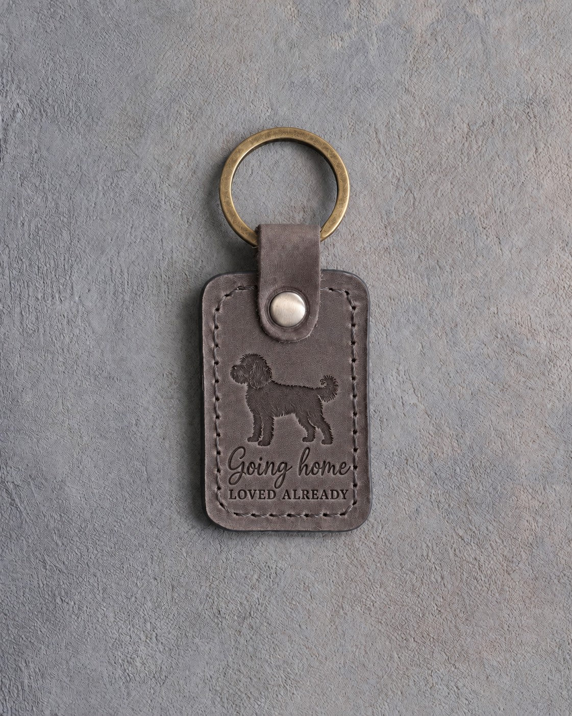 Country gray leather keychain debossed with a cockapoo above Going home and LOVED ALREADY, on gray concrete
