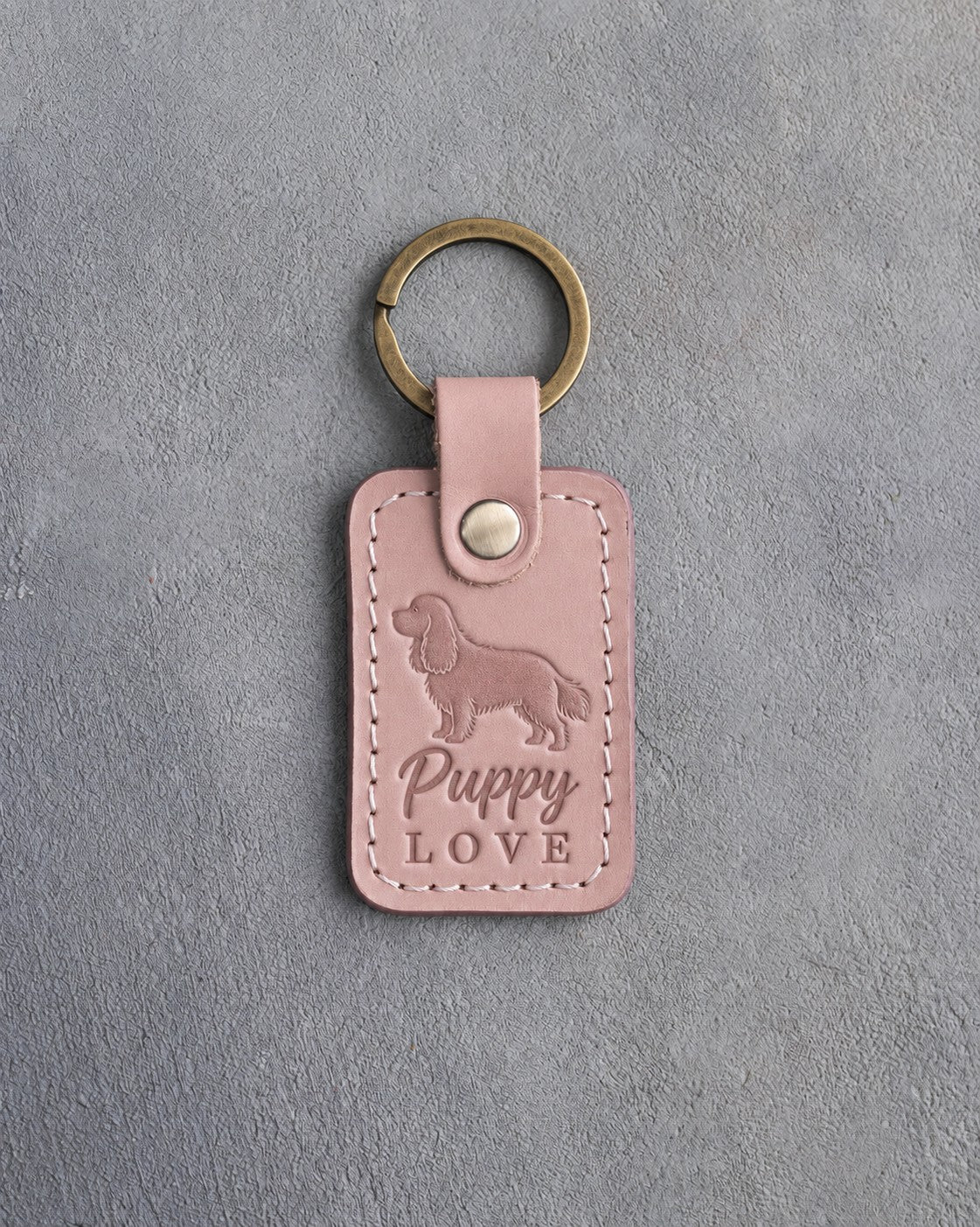 Blush pink leather keychain debossed with a golden retriever and the words Puppy LOVE, on gray concrete