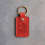 Poppy red leather keychain debossed with a cat pushing a mug off its paw above the words Pushed it OFF THE TABLE