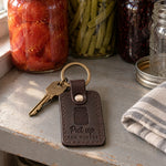 Dark brown Put Up for Winter keychain on a gray painted pantry shelf in front of jars of home-canned tomatoes and beans
