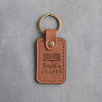 Caramel leather keychain debossed with an open book above Raised a and READER, on gray concrete