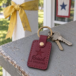 Wine red Raised a Soldier keychain on a parent's key ring resting on a folded letter from basic training