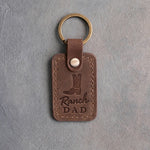 Sicilian brown leather keychain debossed with a cowboy boot above Ranch and DAD, on gray plaster