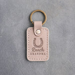 Gray sand leather keychain debossed with a heels-up horseshoe above Ranch and GRANDMA, on gray plaster