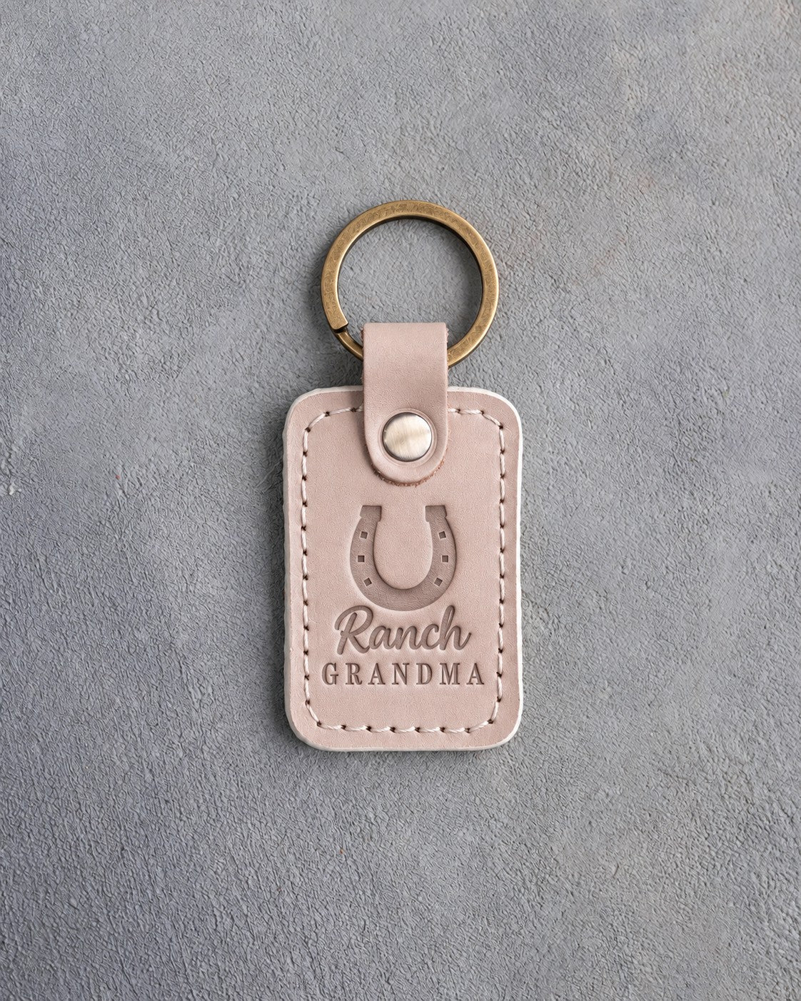 Gray sand leather keychain debossed with a heels-up horseshoe above Ranch and GRANDMA, on gray plaster