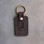 Dark espresso leather keychain debossed with a cowboy boot above Ranch and GRANDPA, on gray plaster