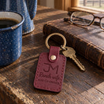 Sangria Ranch wife AND CO-OWNER keychain resting on a closed leather ledger on a dark oak kitchen table