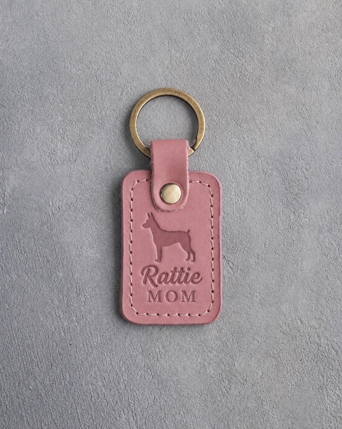 Parisian Blossom pink leather keychain debossed with a Rat Terrier silhouette and the words Rattie MOM, on gray concrete