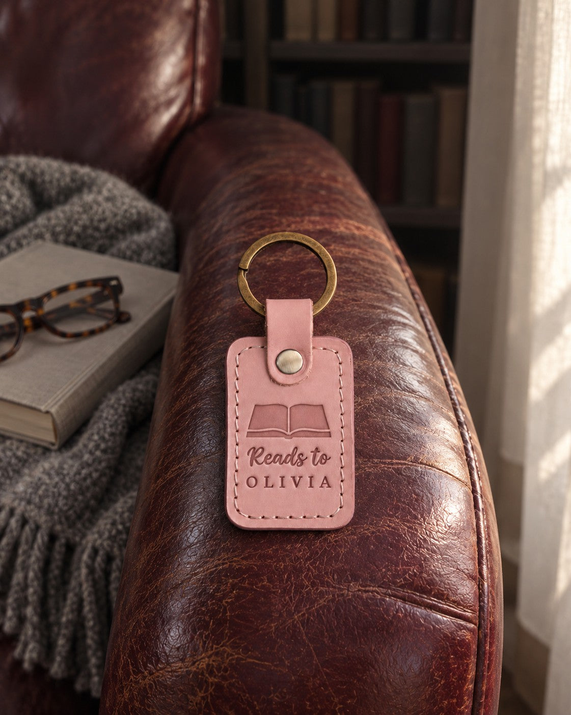 Pink Reads to OLIVIA keychain on an armchair arm beside a picture book and folded reading glasses