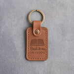 Caramel leather keychain debossed with an open book above Reads to me and GRANDPA, on gray concrete