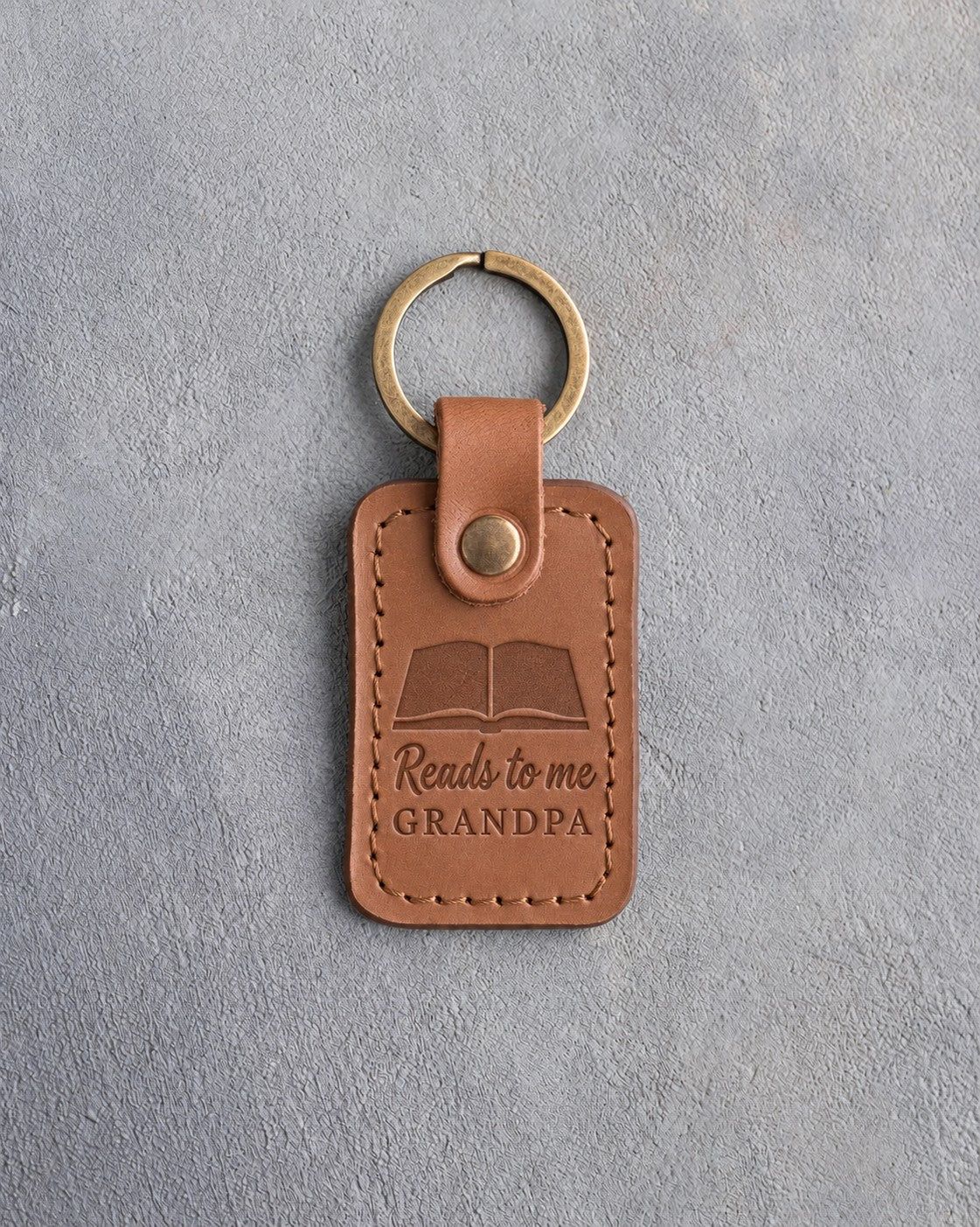 Caramel leather keychain debossed with an open book above Reads to me and GRANDPA, on gray concrete