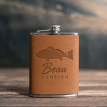 Caramel leather-wrapped hip flask debossed with a redfish above Beau and REDFISH, on a wooden table