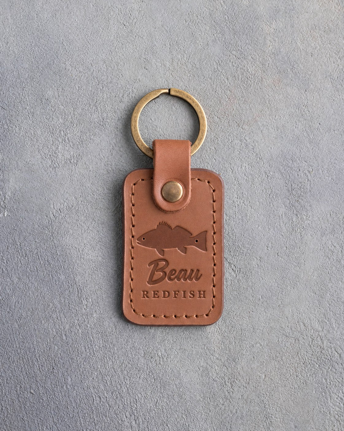 Caramel leather keychain debossed with a redfish above Beau and REDFISH, on gray plaster