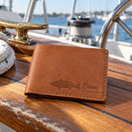 Caramel Beau REDFISH bifold wallet in full-grain leather on the worn teak cockpit table of a sailboat beside a coiled white dock line