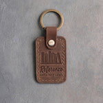 Sicilian brown leather keychain debossed with a shelf of books above Reference and DOES NOT LEND, on gray concrete
