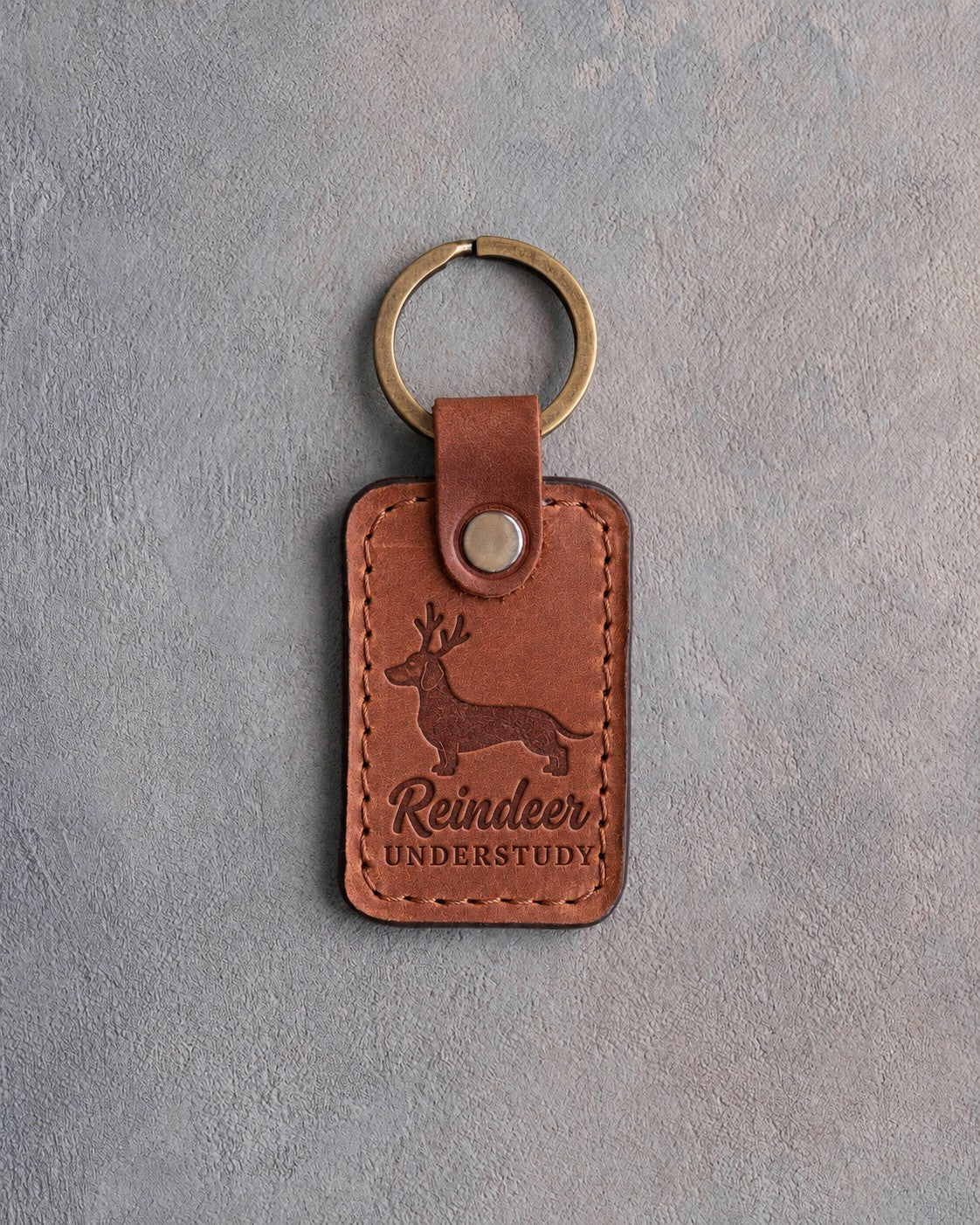 Arizona tan leather keychain debossed with a dachshund wearing antlers and the words Reindeer UNDERSTUDY, on gray concrete