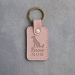Blush pink leather keychain debossed with a sitting mixed-breed dog and the words Rescue MOM, on gray concrete