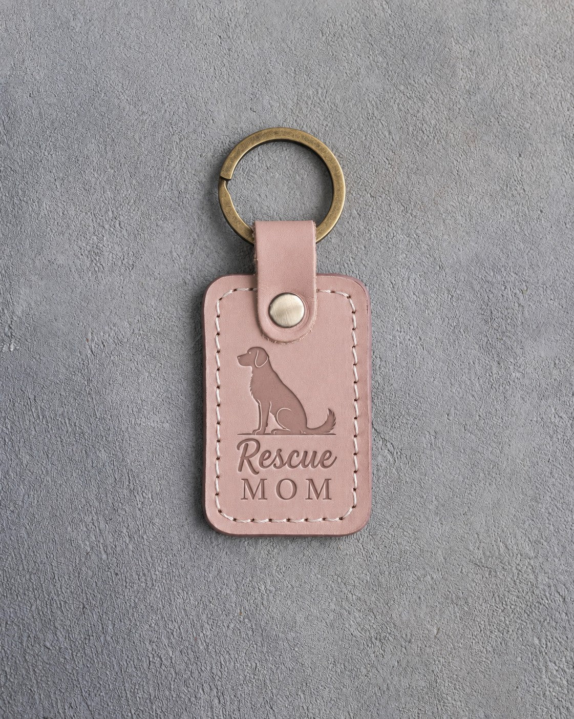Blush pink leather keychain debossed with a sitting mixed-breed dog and the words Rescue MOM, on gray concrete