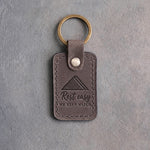 Country gray leather keychain debossed with a folded flag above the words Rest easy WE KEEP WATCH, on gray concrete