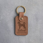 Caramel leather keychain debossed with a Portuguese water dog and the words Retired DECKHAND, on gray concrete