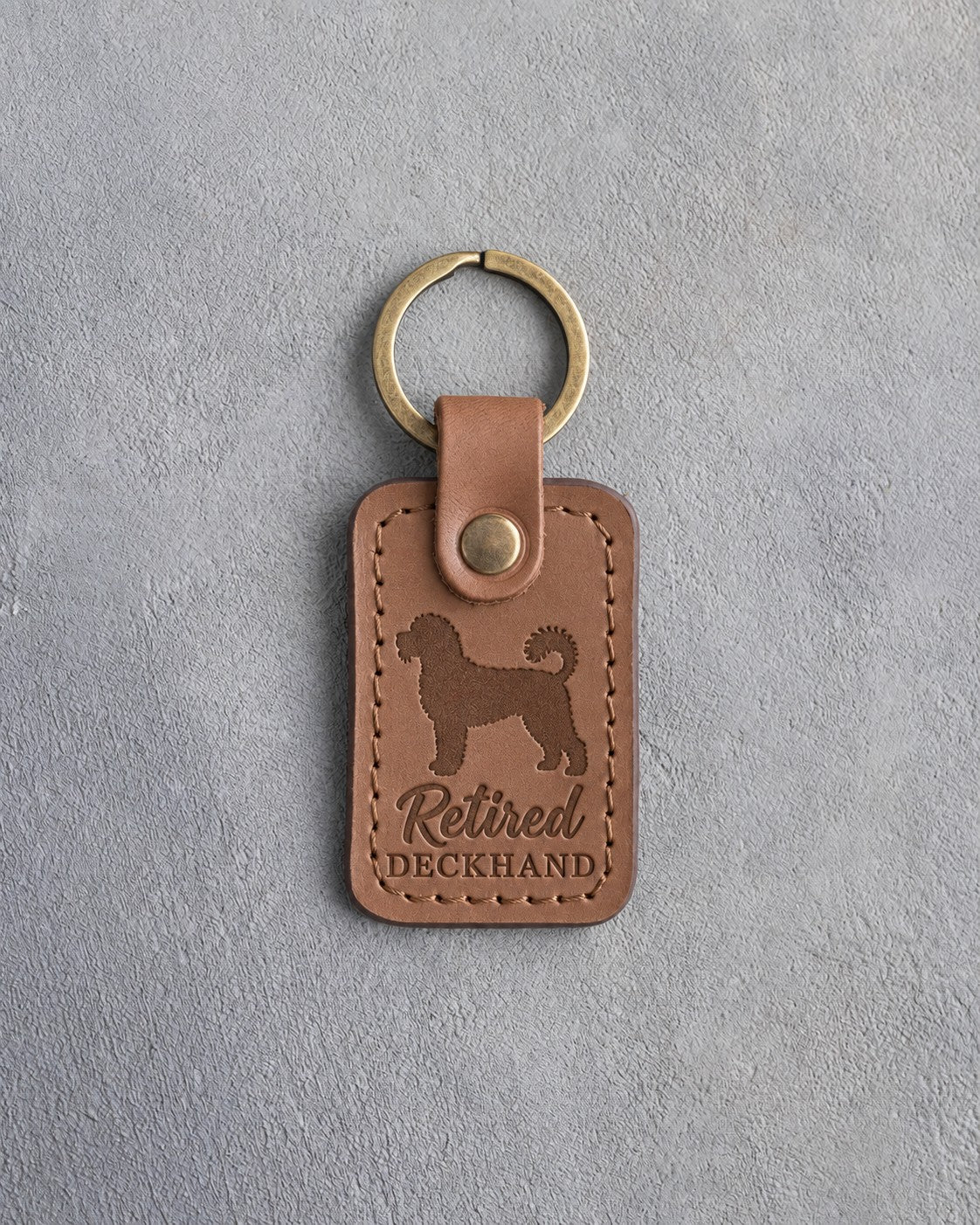 Caramel leather keychain debossed with a Portuguese water dog and the words Retired DECKHAND, on gray concrete