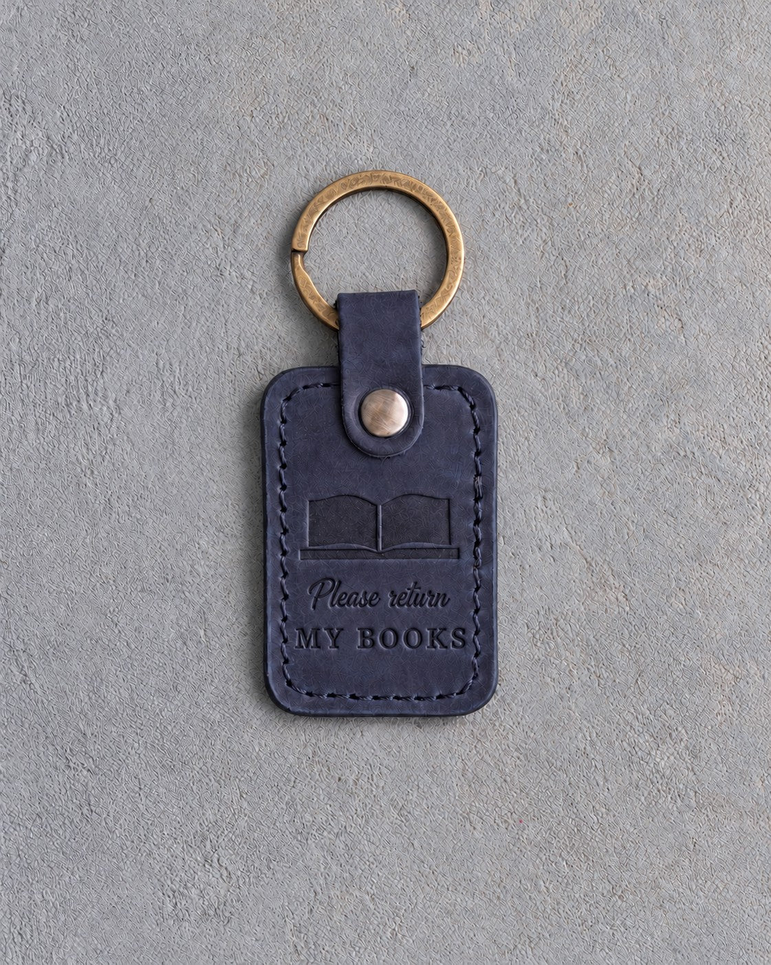 Blueberry navy leather keychain debossed with an open book above Please return and MY BOOKS, on gray concrete