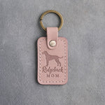 Blush pink leather keychain debossed with a Rhodesian Ridgeback silhouette and the words Ridgeback MOM, on gray concrete
