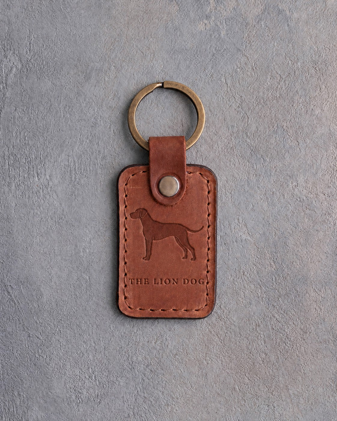 Arizona tan leather keychain debossed with a Rhodesian Ridgeback silhouette above THE LION DOG, on gray concrete