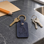 Navy Right Here Michigan keychain held in an open palm beside a lake shore on a cool morning
