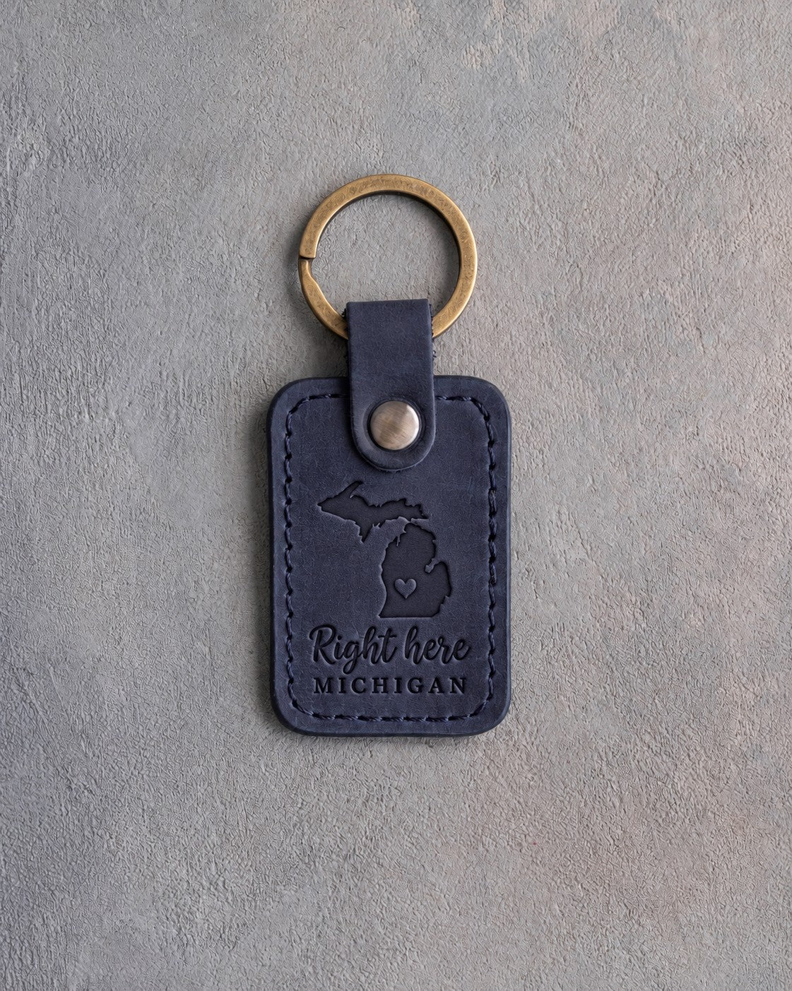 Blueberry navy leather keychain debossed with Michigan's two peninsulas and a heart at Grand Rapids above Right here and MICHIGAN, on gray concrete