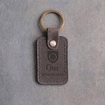Country gray leather keychain debossed with a shield badge holding a wedding band, above Our and RING BEARER, on gray concrete