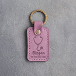 Lilac leather keychain debossed with a stethoscope above the name Megan and RN SINCE 2026, on gray plaster