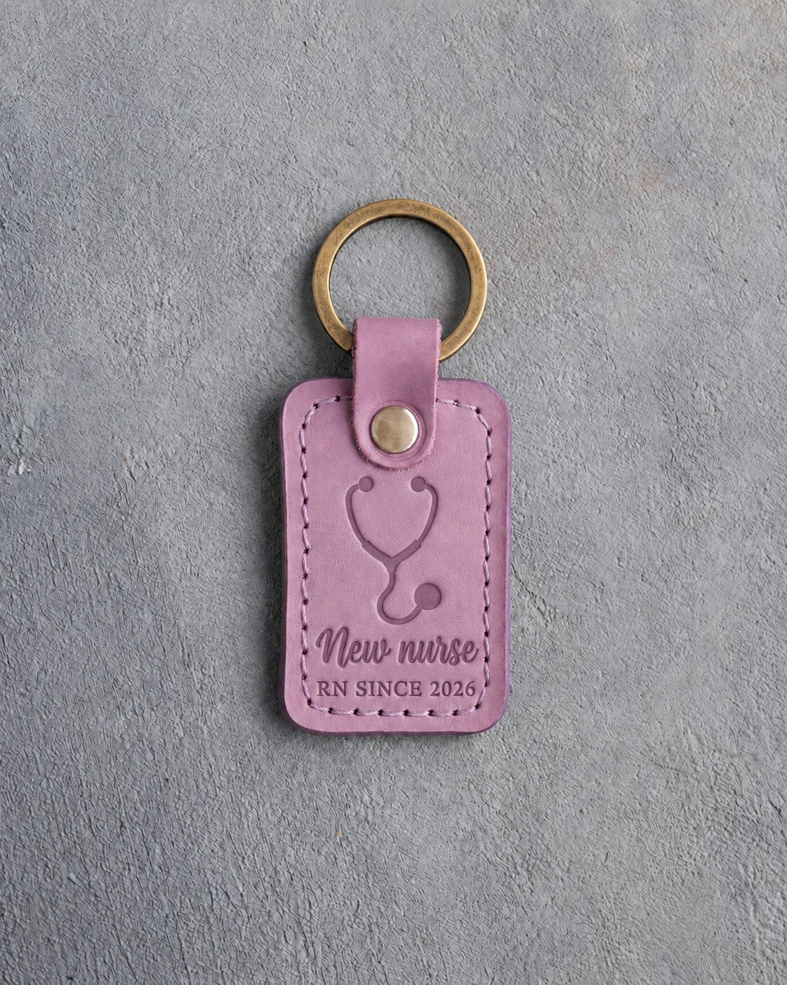 Lilac leather keychain debossed with a stethoscope above the words New nurse and RN SINCE 2026, on gray concrete