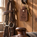 Sicilian brown Rodeo DAD keychain hanging from a forged iron bridle hook on a pine tack room wall beside a worn headstall