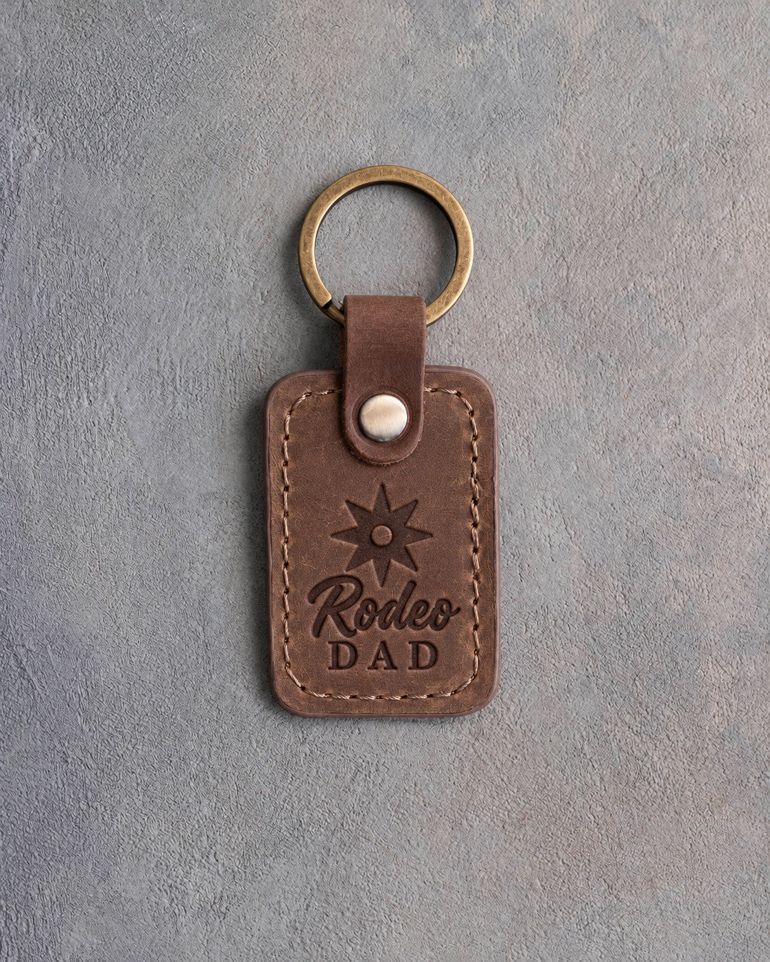 Sicilian brown leather keychain debossed with a spur rowel above Rodeo and DAD, on gray plaster