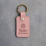 Blush pink leather keychain debossed with a spur rowel above Rodeo and GRANDMA, on gray plaster