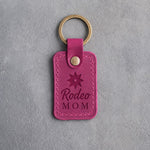 Fuchsia leather keychain debossed with a spur rowel above Rodeo and MOM, on gray plaster