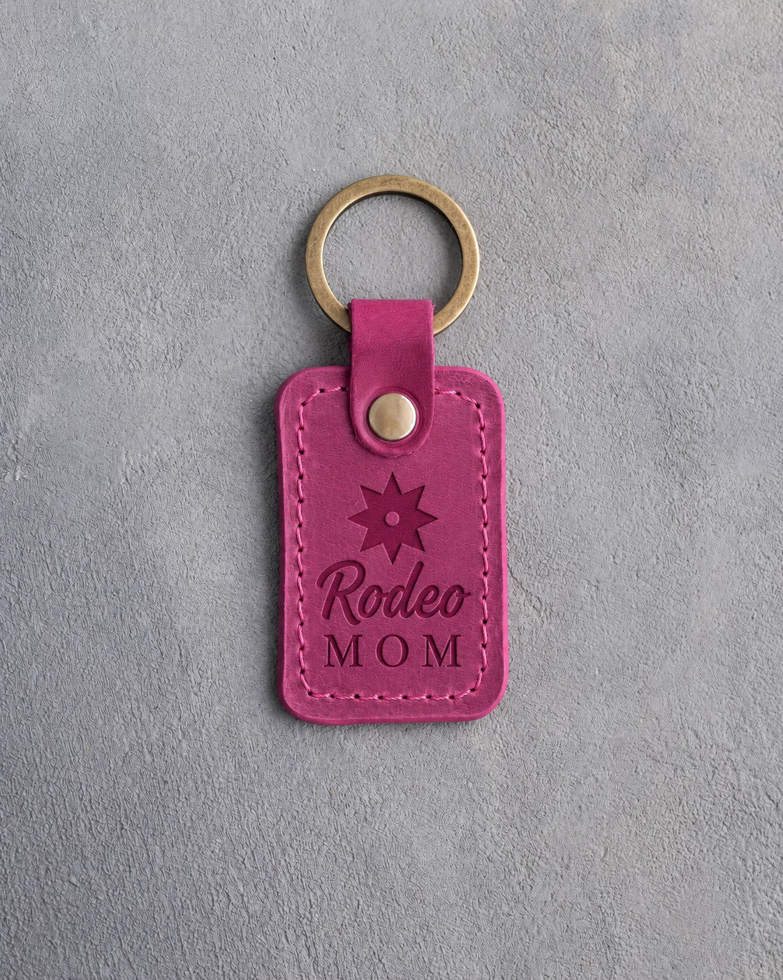 Fuchsia leather keychain debossed with a spur rowel above Rodeo and MOM, on gray plaster