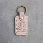 Gray sand leather keychain debossed with a baseball and the words Rookie year SEASON 2026, on gray plaster