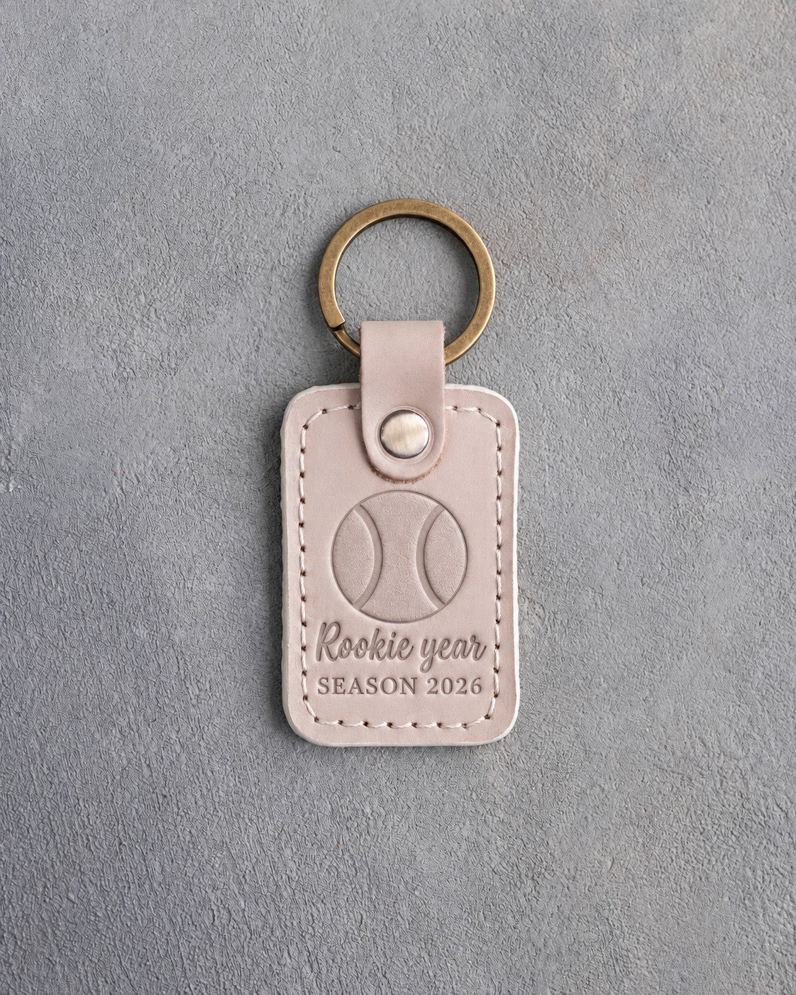 Gray sand leather keychain debossed with a baseball and the words Rookie year SEASON 2026, on gray plaster