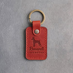 Poppy red leather keychain debossed with a Rat Terrier silhouette and the words Roosevelt APPROVED, on gray concrete
