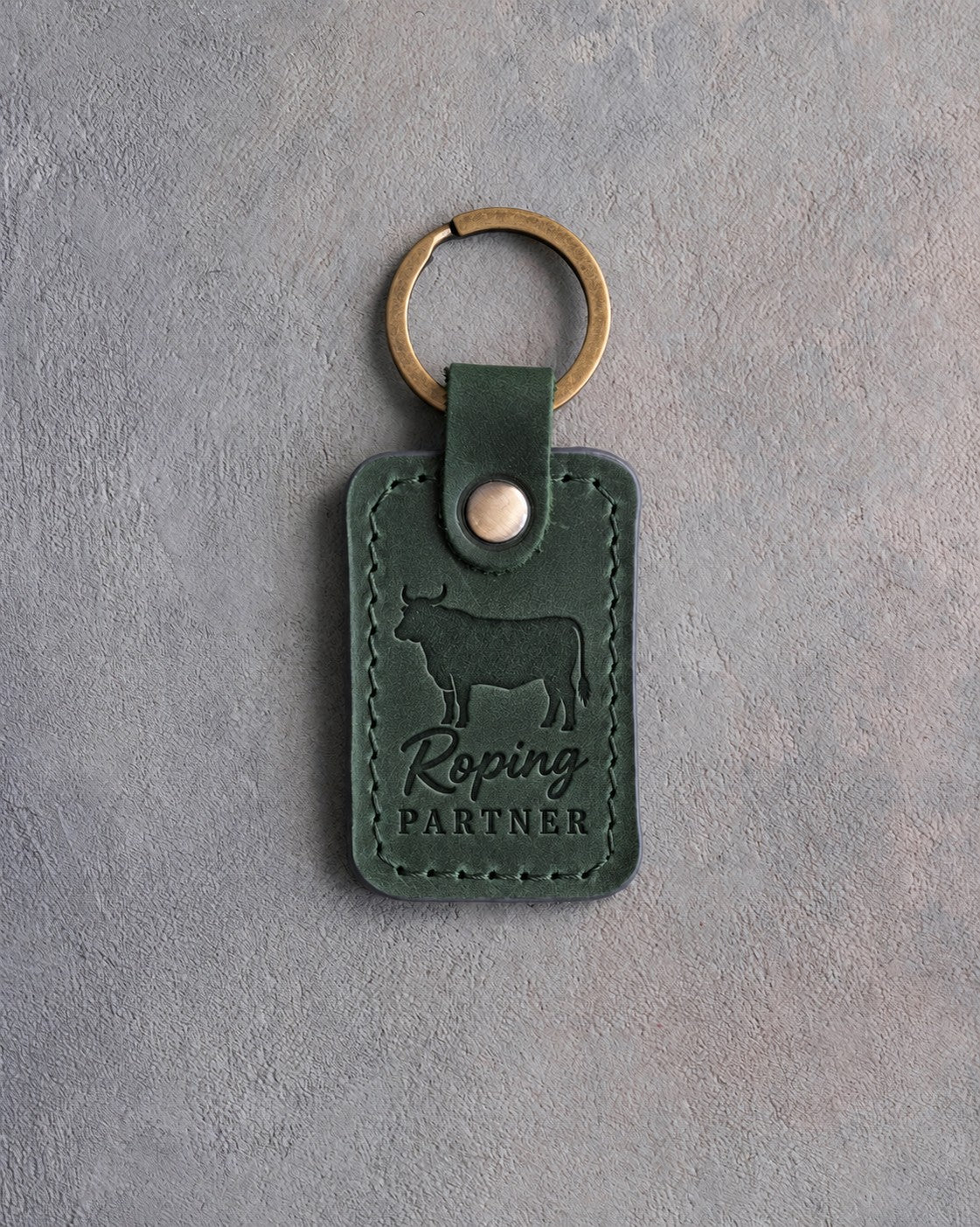 Forest green leather keychain debossed with a steer silhouette above Roping and PARTNER, on gray plaster