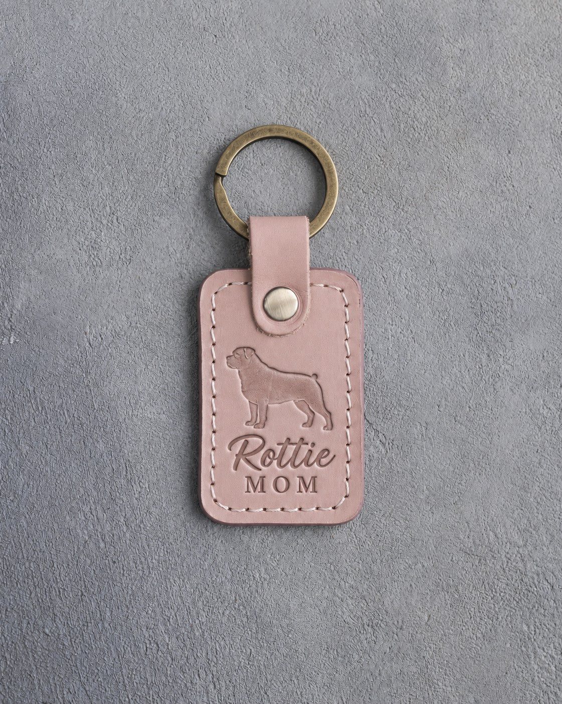 Blush pink leather keychain debossed with a Rottweiler silhouette and the words Rottie MOM, on gray concrete