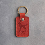 Poppy red leather keychain debossed with a Cavalier King Charles Spaniel silhouette and the words Royal LAP WARMER, on gray concrete