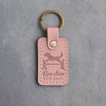 Blush pink leather keychain debossed with a dog leaping over an agility jump and the words Run clean RUN FAST, on gray concrete