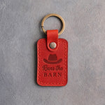 Poppy red leather keychain debossed with a cowboy hat above Runs the and BARN, on gray plaster
