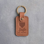 Caramel leather keychain debossed with a home plate and the words Safe AT HOME, on gray plaster